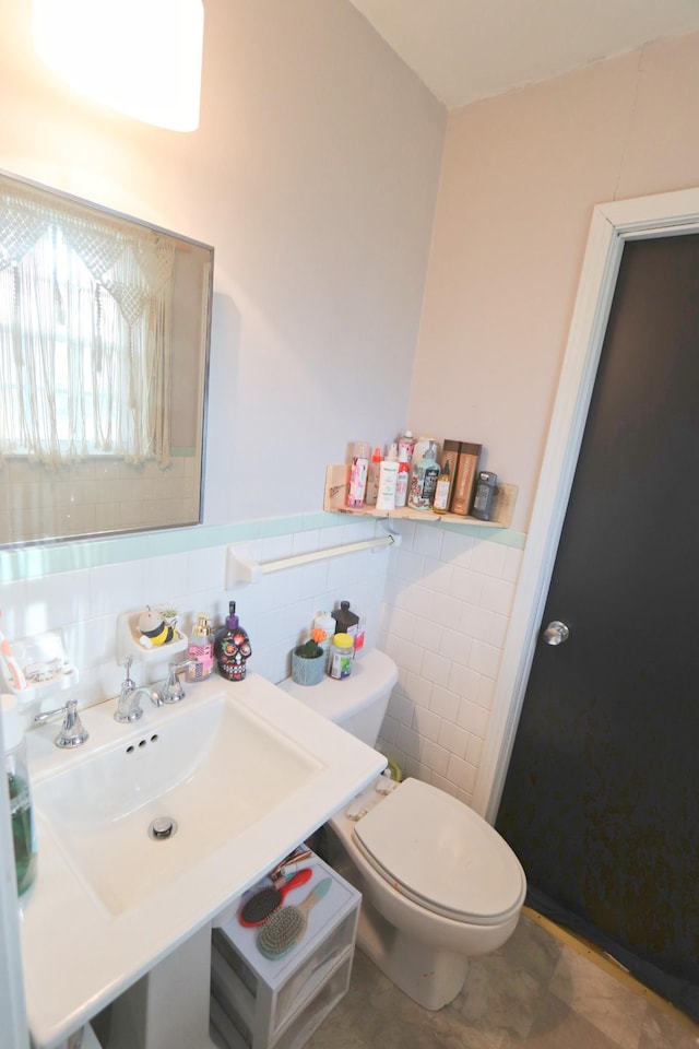 bathroom featuring toilet, a wainscoted wall, tile walls, and a sink
