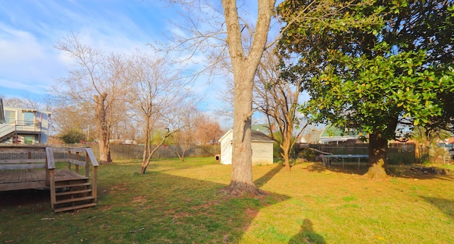 view of yard with a wooden deck, a trampoline, an outbuilding, a fenced backyard, and a storage unit
