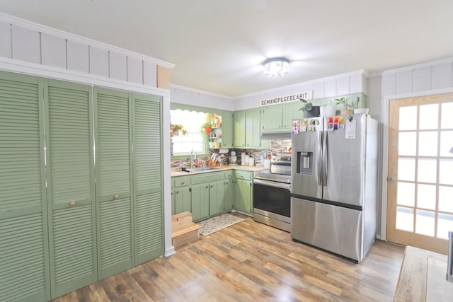 kitchen with green cabinetry, crown molding, a sink, appliances with stainless steel finishes, and light countertops