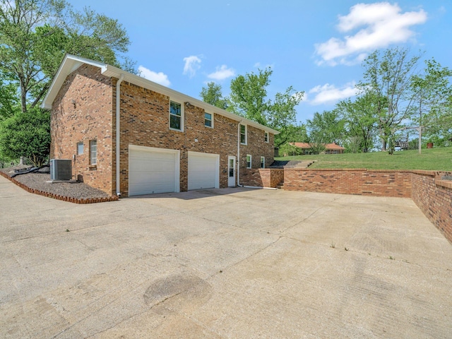 view of home's exterior featuring brick siding, central AC unit, driveway, and an attached garage