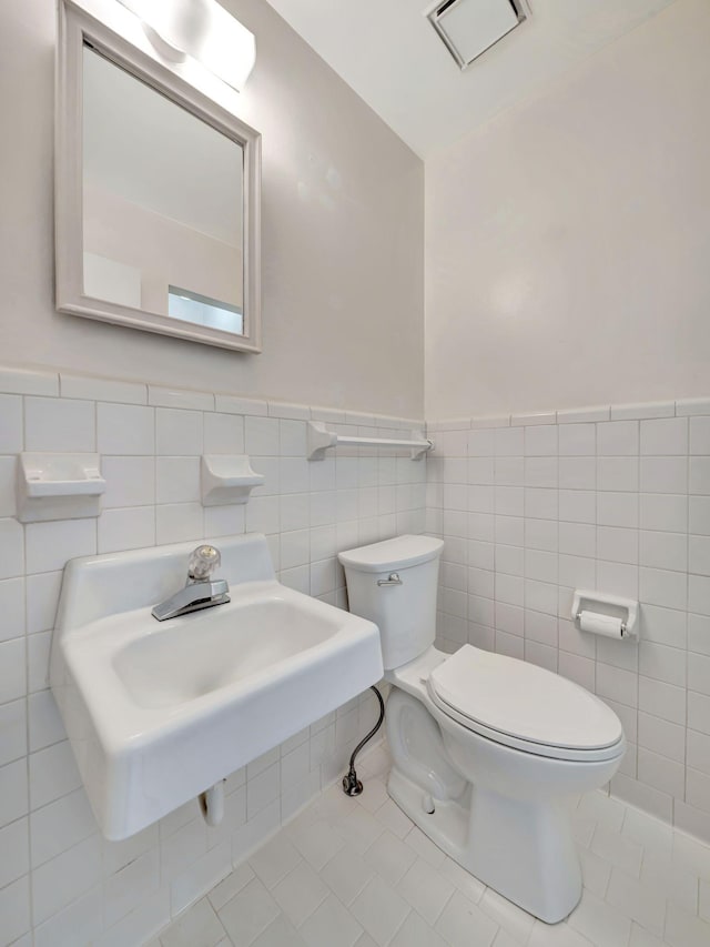half bathroom with tile patterned flooring, wainscoting, tile walls, toilet, and a sink