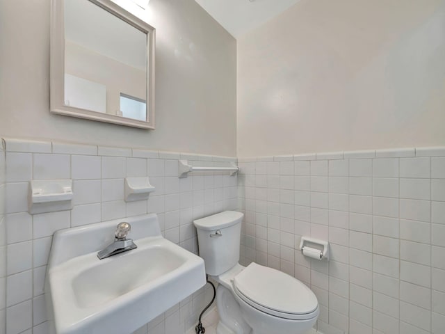 bathroom with toilet, tile walls, a sink, and wainscoting