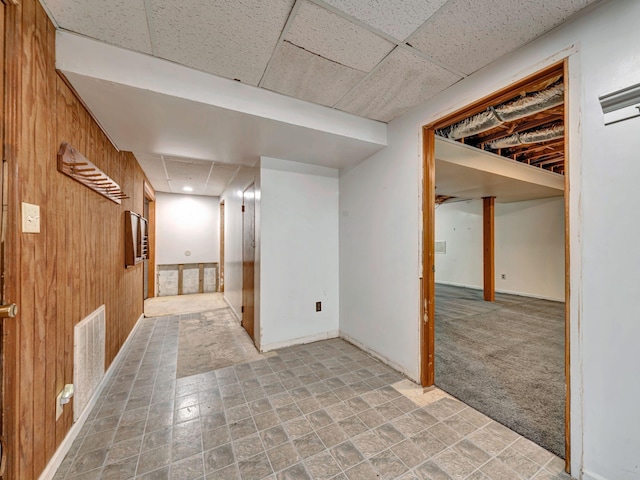 finished basement featuring wooden walls, visible vents, a drop ceiling, and carpet