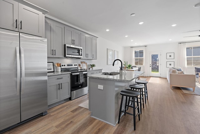 kitchen with a sink, appliances with stainless steel finishes, a kitchen bar, wood finished floors, and gray cabinets