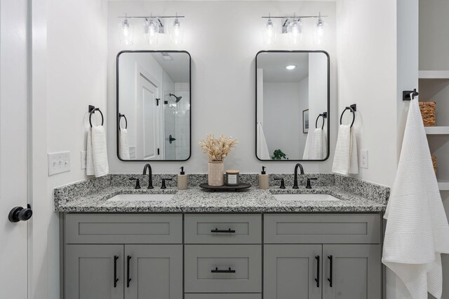 bathroom with tiled shower, double vanity, and a sink