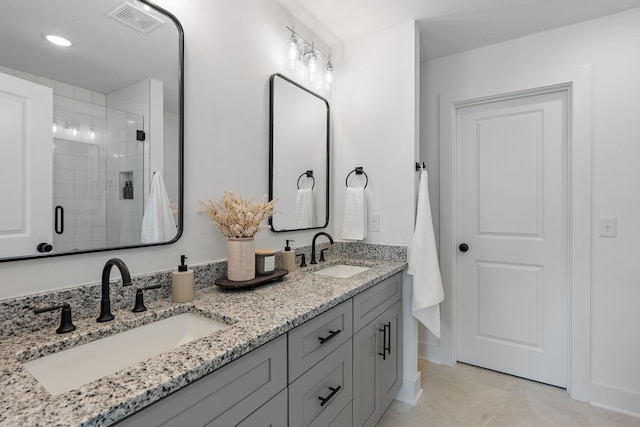 bathroom with a stall shower, double vanity, a sink, and visible vents