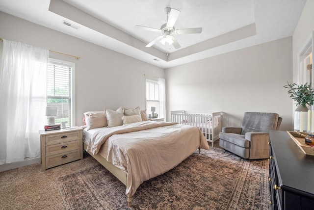 bedroom with ceiling fan, visible vents, multiple windows, and a raised ceiling