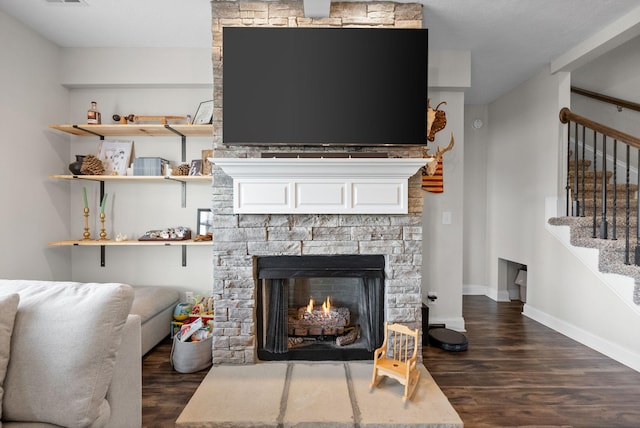 interior details with baseboards, visible vents, a stone fireplace, and wood finished floors