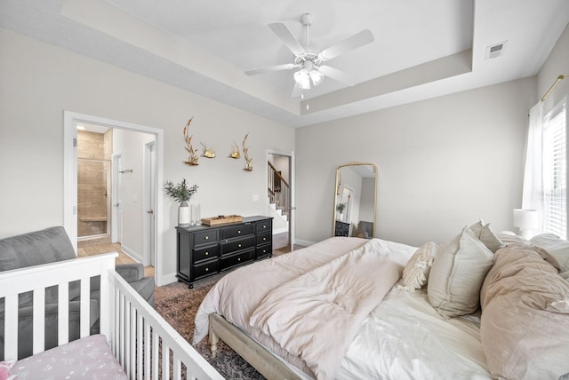 bedroom featuring visible vents, arched walkways, baseboards, a tray ceiling, and ensuite bath