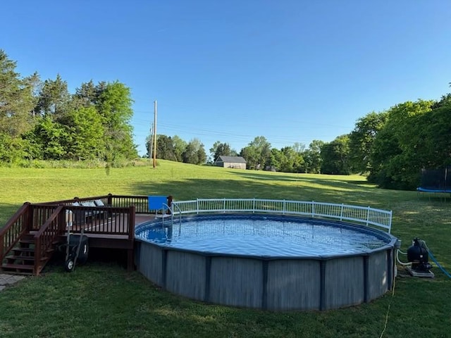pool featuring a trampoline, a yard, and a wooden deck