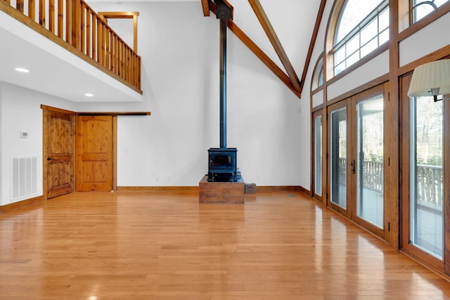 unfurnished living room featuring visible vents, light wood-type flooring, high vaulted ceiling, and a wood stove