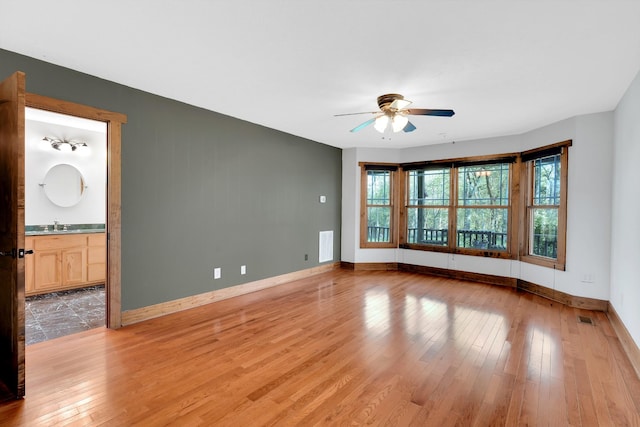 empty room featuring a sink, light wood-type flooring, a ceiling fan, visible vents, and baseboards