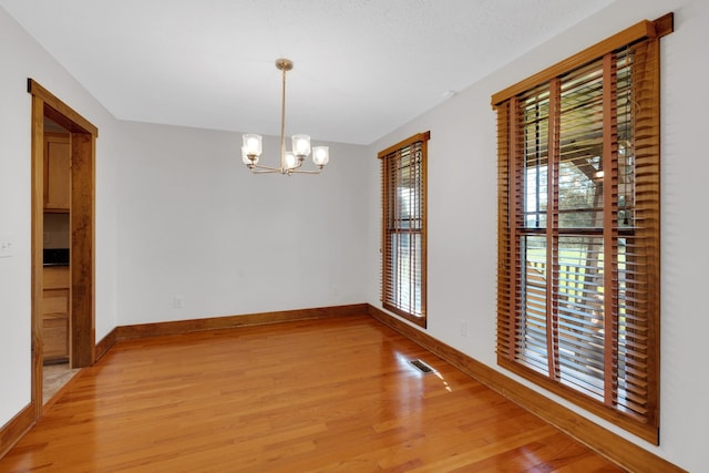 unfurnished dining area with a notable chandelier, visible vents, baseboards, and light wood-type flooring