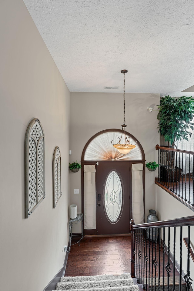 foyer entrance with a textured ceiling, stairs, baseboards, visible vents, and hardwood / wood-style flooring