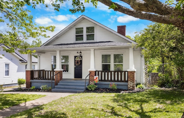 bungalow-style home with a chimney, covered porch, and a front lawn