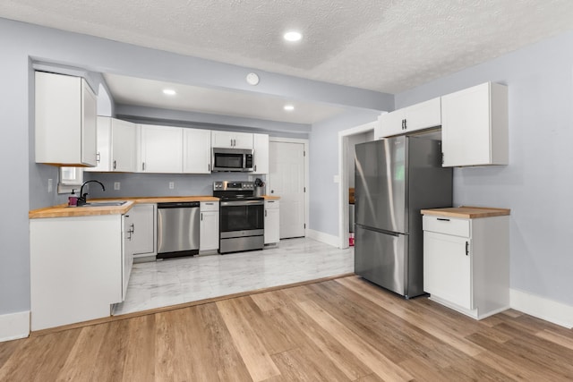 kitchen with a sink, wood counters, white cabinetry, baseboards, and appliances with stainless steel finishes