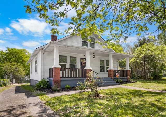 view of front of home featuring a chimney, fence, covered porch, and a front lawn