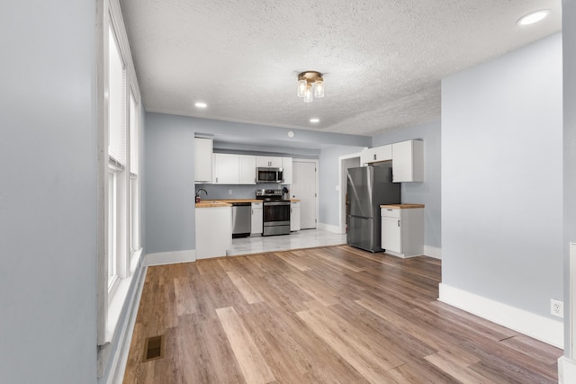 unfurnished living room with a textured ceiling, a sink, visible vents, light wood-style floors, and baseboards