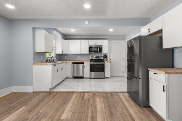 kitchen with wood counters, a sink, appliances with stainless steel finishes, light wood-type flooring, and recessed lighting