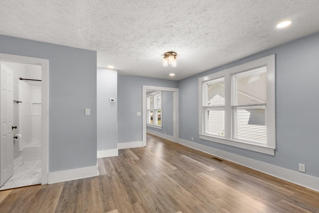 unfurnished living room with recessed lighting, wood finished floors, baseboards, visible vents, and a textured ceiling