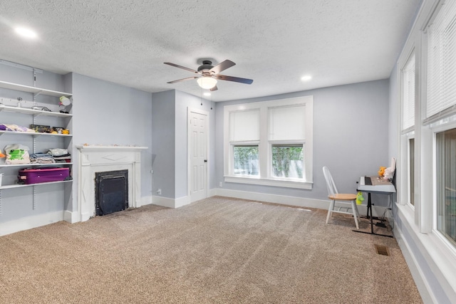 carpeted living area with a fireplace, visible vents, a healthy amount of sunlight, and a ceiling fan