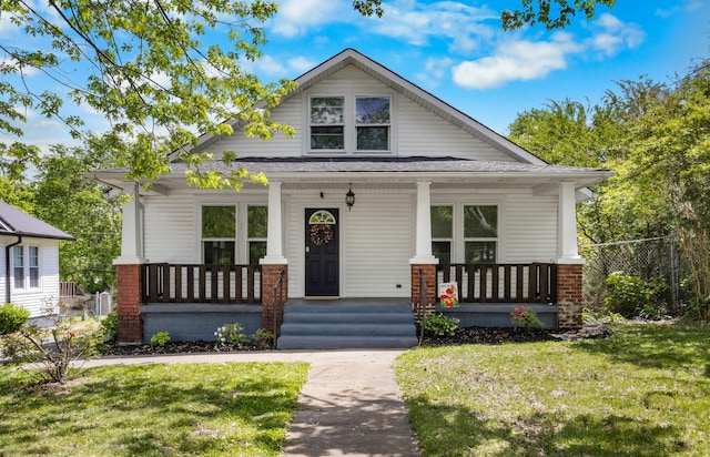 bungalow-style home featuring a front lawn, fence, covered porch, and brick siding