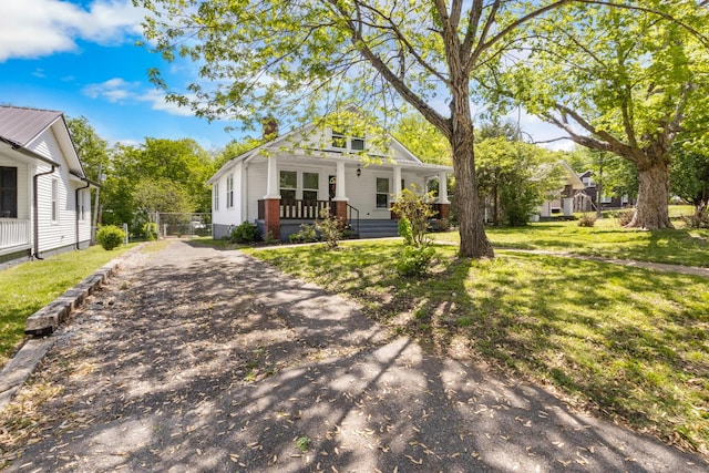 bungalow with covered porch, aphalt driveway, a chimney, and a front lawn