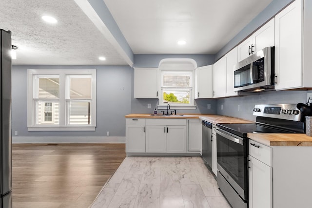 kitchen featuring recessed lighting, a sink, wood counters, white cabinets, and appliances with stainless steel finishes
