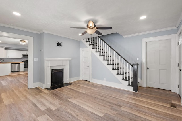 unfurnished living room with ceiling fan, stairway, light wood-style flooring, and a fireplace with flush hearth