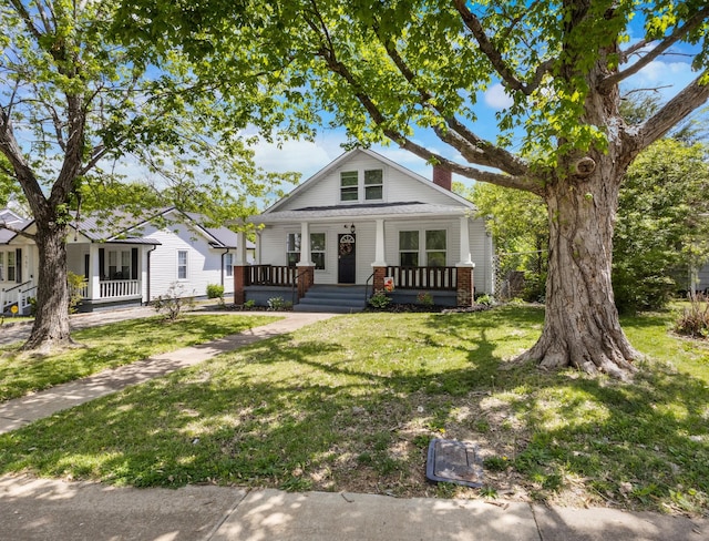 bungalow-style home featuring covered porch, a chimney, and a front lawn
