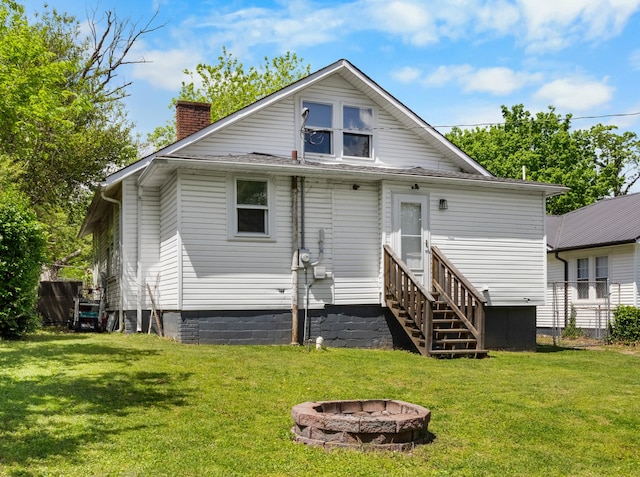 back of house featuring a chimney, an outdoor fire pit, entry steps, and a yard