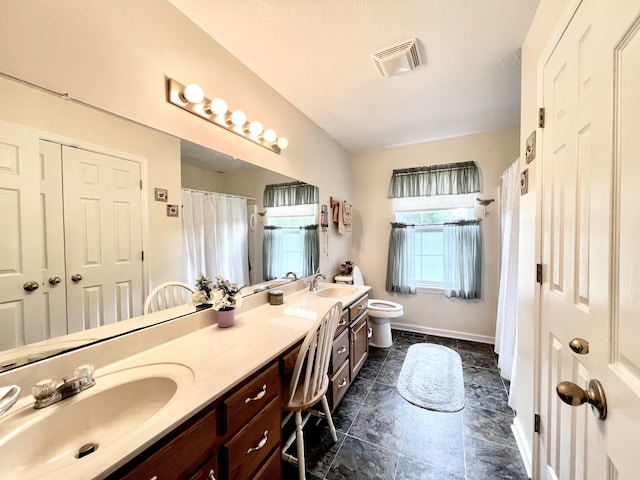 full bath with visible vents, toilet, double vanity, and a sink