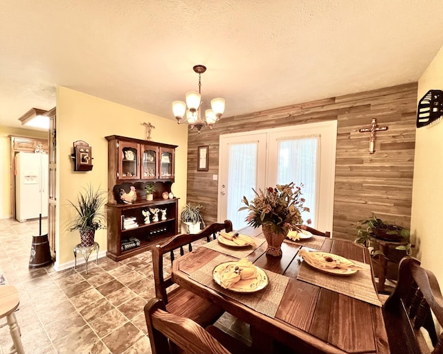 dining area featuring light tile patterned flooring, a textured ceiling, an inviting chandelier, and wood walls