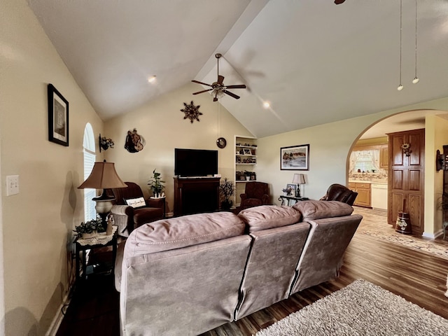 living area featuring lofted ceiling, wood finished floors, a ceiling fan, and arched walkways