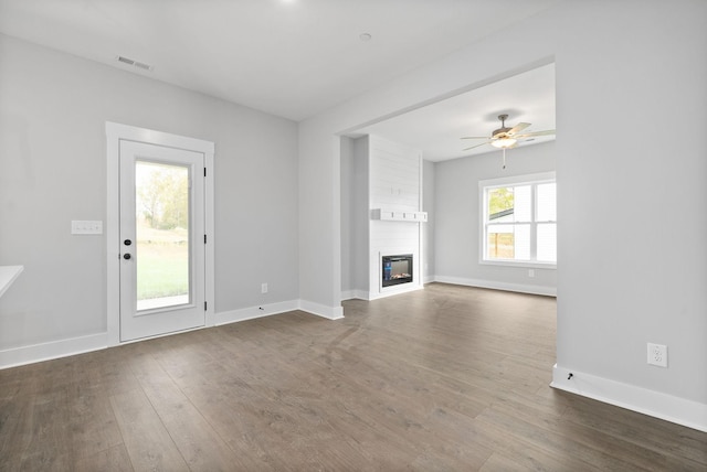 unfurnished living room with dark wood-type flooring, a large fireplace, a ceiling fan, and baseboards