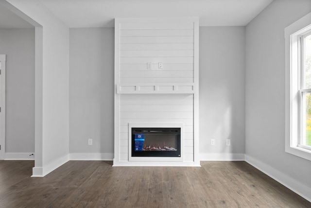 unfurnished living room featuring a large fireplace, wood finished floors, and baseboards