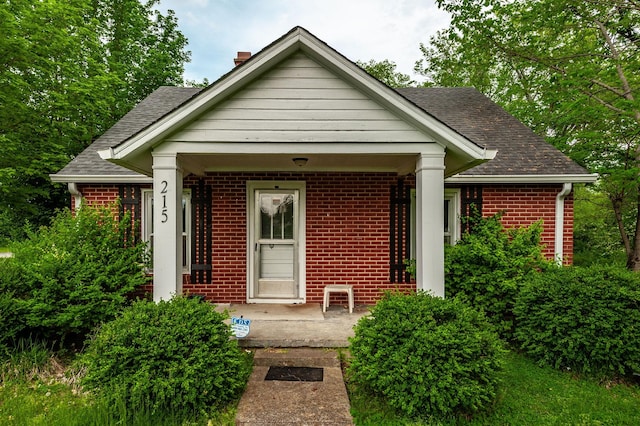 view of front of home featuring a chimney, brick siding, and roof with shingles