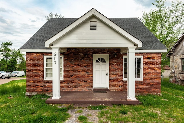 view of front of property with brick siding, fence, a front lawn, and roof with shingles