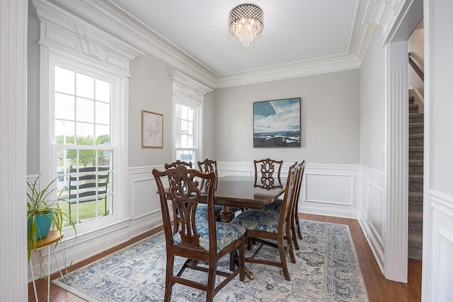 dining space featuring ornamental molding, wainscoting, wood finished floors, stairway, and a notable chandelier