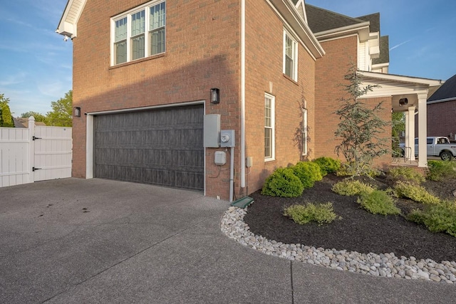view of side of home featuring fence, brick siding, a garage, a gate, and concrete driveway