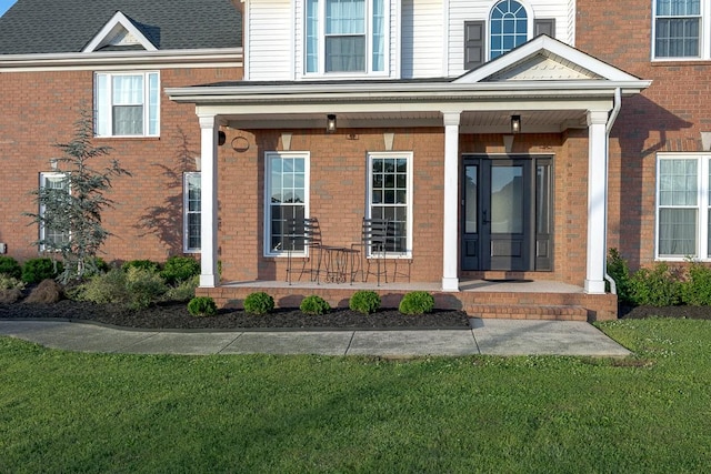 entrance to property featuring a yard, a porch, and brick siding
