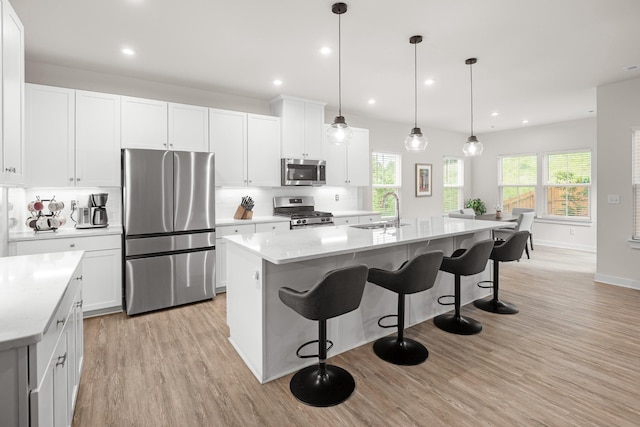 kitchen featuring appliances with stainless steel finishes, a center island with sink, a sink, light wood finished floors, and a breakfast bar