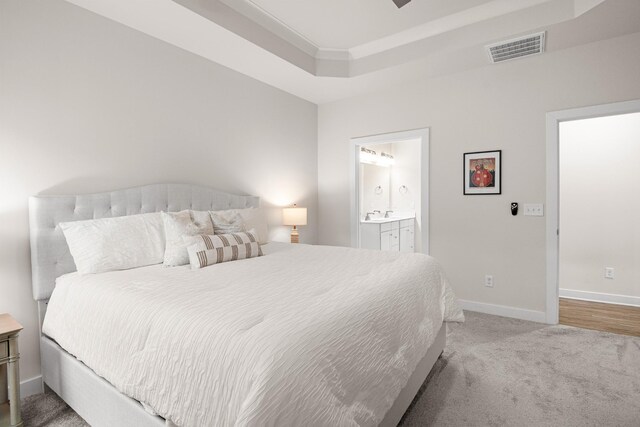 carpeted bedroom with connected bathroom, baseboards, visible vents, and a raised ceiling
