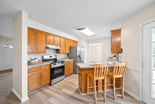 3844 Marla Cir, Clarksville, TN 37042 - kitchen with under cabinet range hood, appliances with stainless steel finishes, brown cabinets, light wood-type flooring, and a peninsula