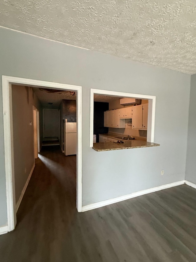 unfurnished living room featuring dark wood-style flooring, baseboards, and a textured ceiling