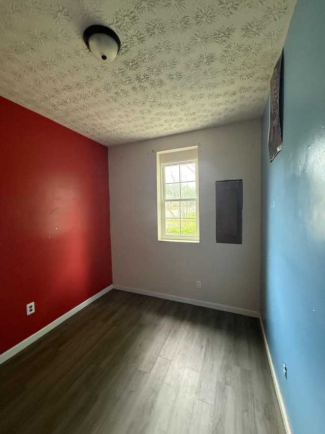 spare room featuring baseboards, wood finished floors, a textured ceiling, and electric panel