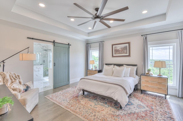 bedroom with recessed lighting, a barn door, light wood finished floors, baseboards, and a tray ceiling
