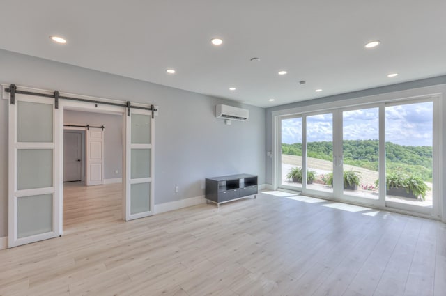 unfurnished room with recessed lighting, a barn door, light wood finished floors, baseboards, and a wall unit AC