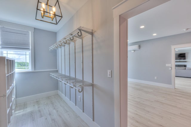 spacious closet with wood finished floors, a wall mounted AC, and a notable chandelier