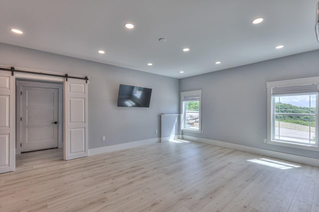 unfurnished living room featuring recessed lighting, light wood-style flooring, a barn door, and baseboards